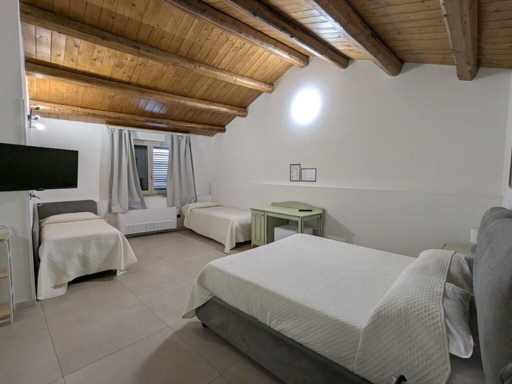 Room with a double bed and single beds under a wooden beamed roof